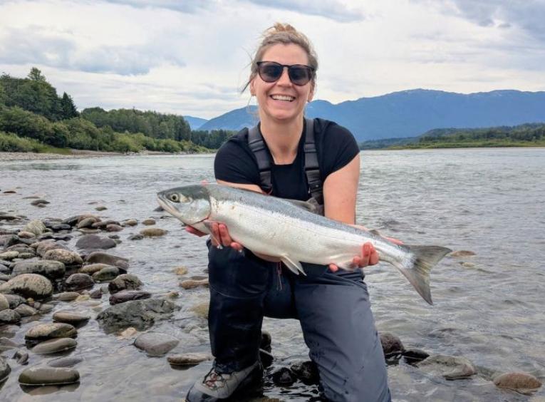 Amanda holding a freshly caught fish on the banks of a river