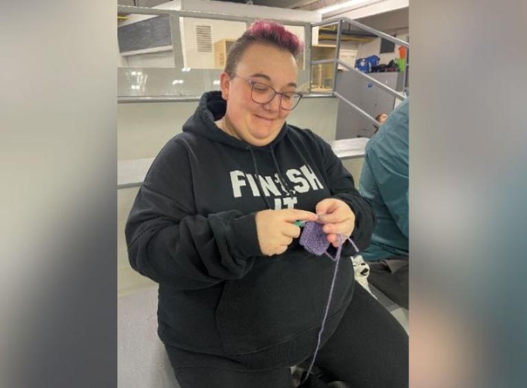 Woman knitting in bleachers at hockey game.