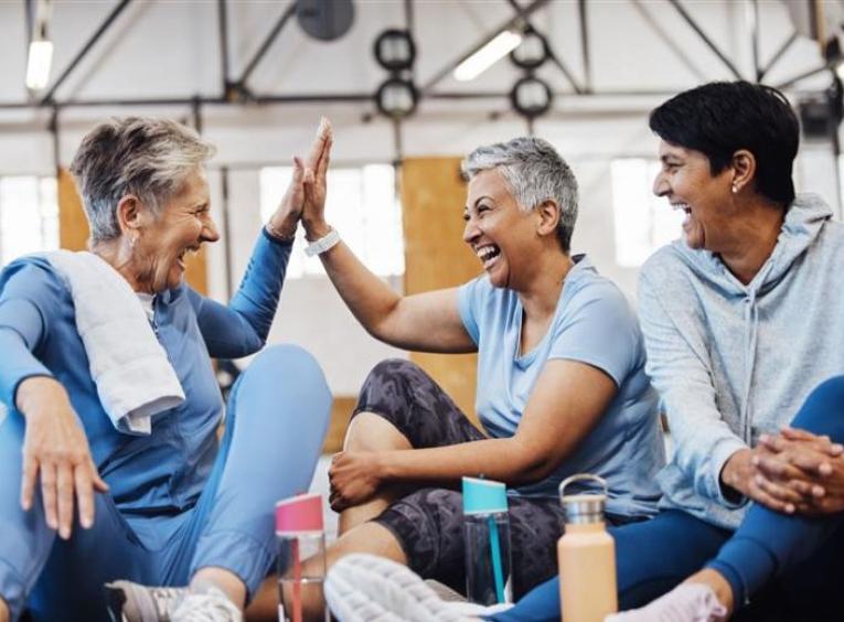 3 women sitting on the floor of an exercise gym laughing