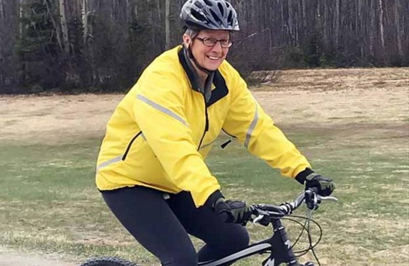 Barb Paterson, smiling in a yellow reflective biking jacket, and riding a bike.