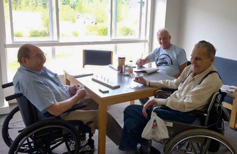 Three elderly men sitting around a table, two in wheelchairs