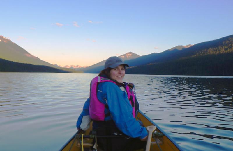 Ibolya is in the front of a canoe on a clam lake, surrounded by mountains.