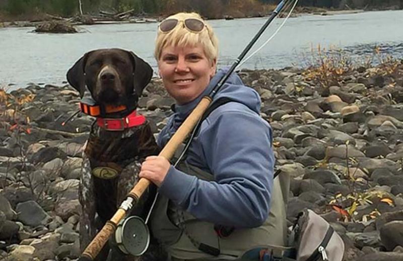 Leah Smith with her dog, Sage, holding a fishing rod near a river.