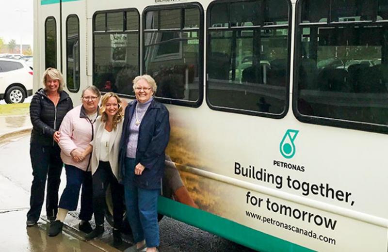 Four women stand in front of the new PETRONAS Canada shuttle bus for Peace Villa.