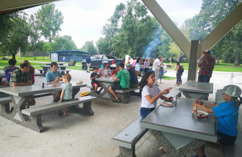 Adults and children sit and eat at picnic benches.