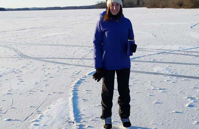 Woman standing on a frozen lake with ice skates on.