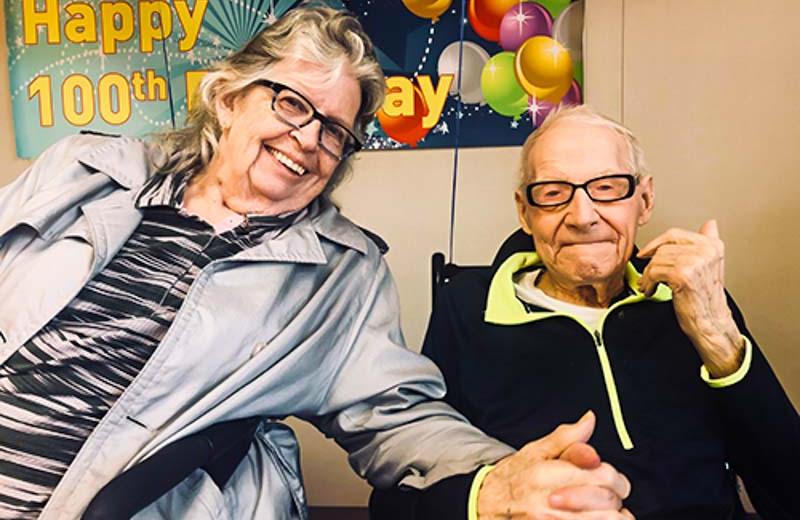 A man celebrating his 100th birthday and holding hands with his wife