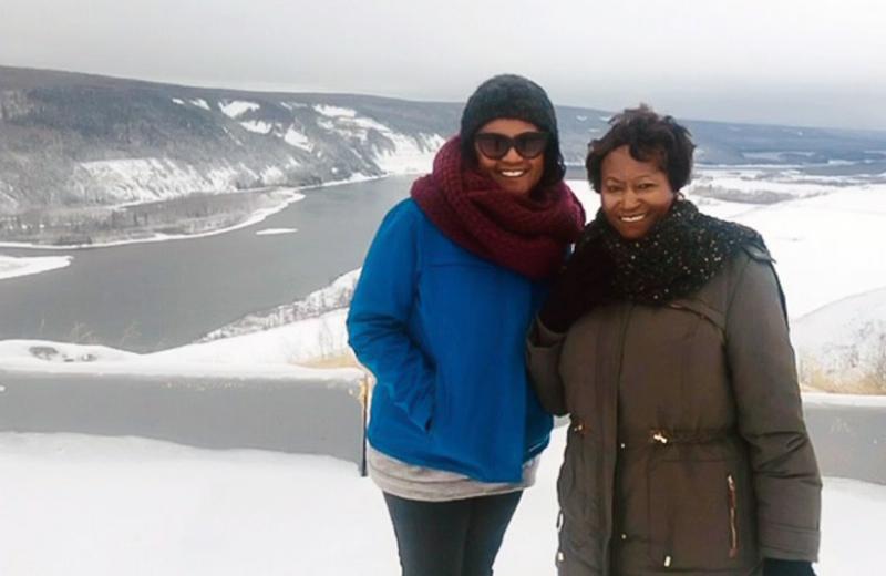 Stella and her mother are bundled up on top of a hill, overlooking other snowy hills and a body of water.