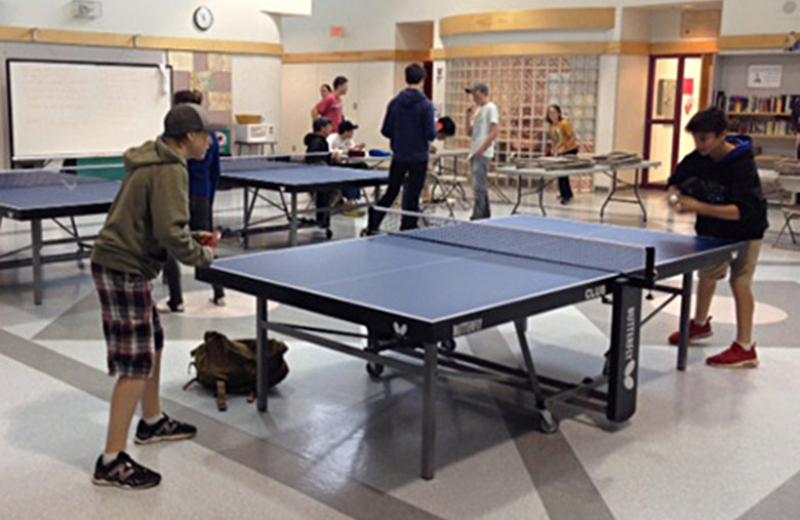 Students playing table tennis in a gym hall.