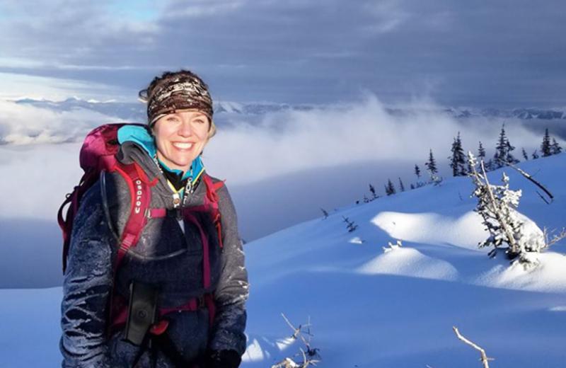 Tanya Carter is pictured on top of a mountain in the snow. In the distance is a snowy mountain range.