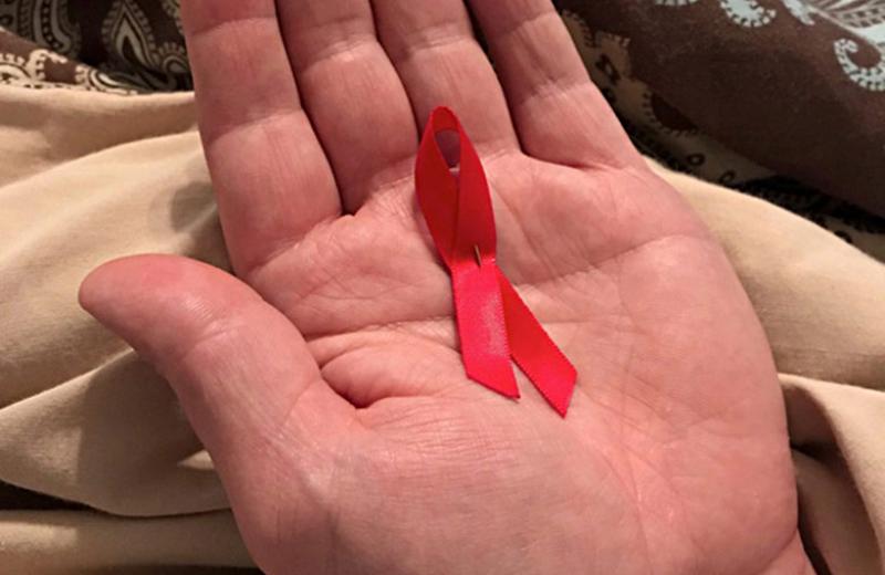 Small red AIDS ribbon in the palm of someone's hand.