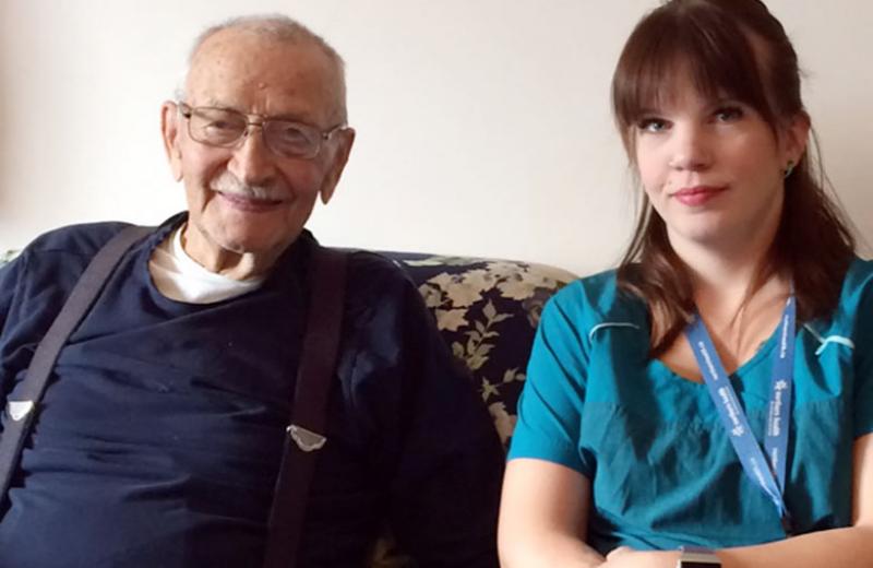 An elderly man and a young woman sit on a couch.