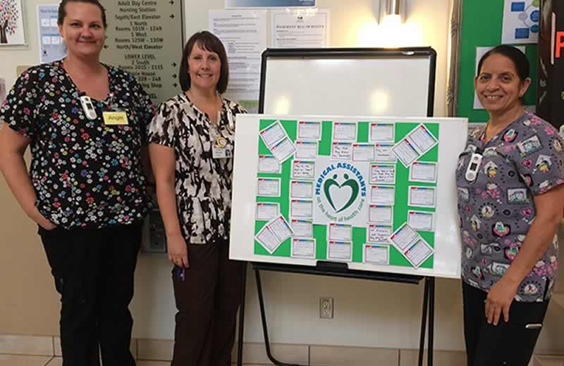 Care aides standing and smiling with thank you board .