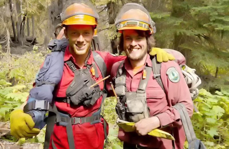 Two young men standing in a forest with their forest firefighting gear on.