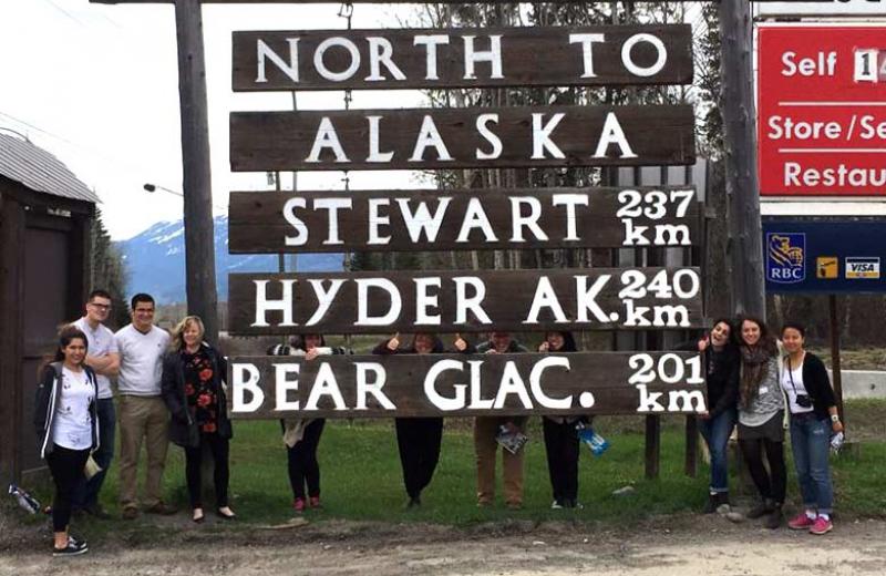 Group standing below a big wooden sign showing towns.