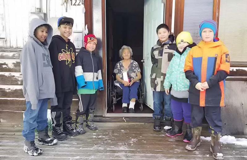 Group of kids and elder standing outside on a house deck in winter.