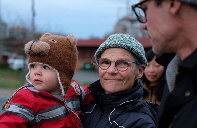 A woman outside holding a toddler boy in a bear toque.