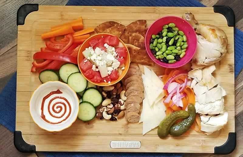 Snack foods on a board including meat, cheese & pickles.