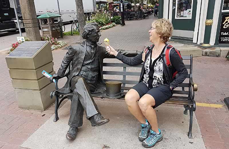 Susan Knoll sitting on a bench with a statue, eating ice cream. 