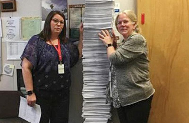 Two women standing with a tall stack of chart copies between them.