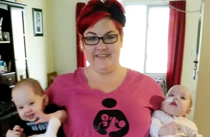 Woman in a pink shirt holding a baby in each arm.