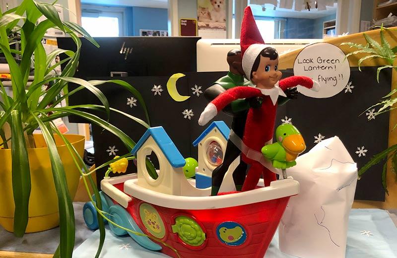 The elf on the shelf is held up by a toy version of the super hero Green Lantern, reenacting a scene from the movie Titanic. 