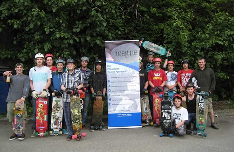 Large group of youth standing with skateboards and wearing helmuts.