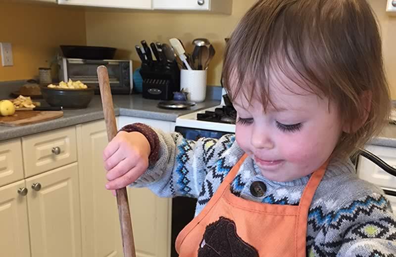 Toddler holding a wooden mixing spoon over a bowl full of oats.
