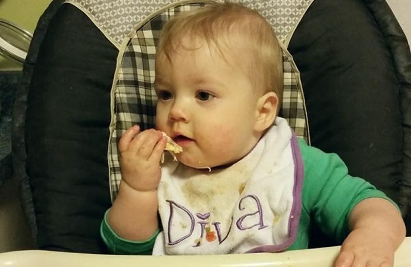 Baby in a high chair wearing a green shirt and a bib.