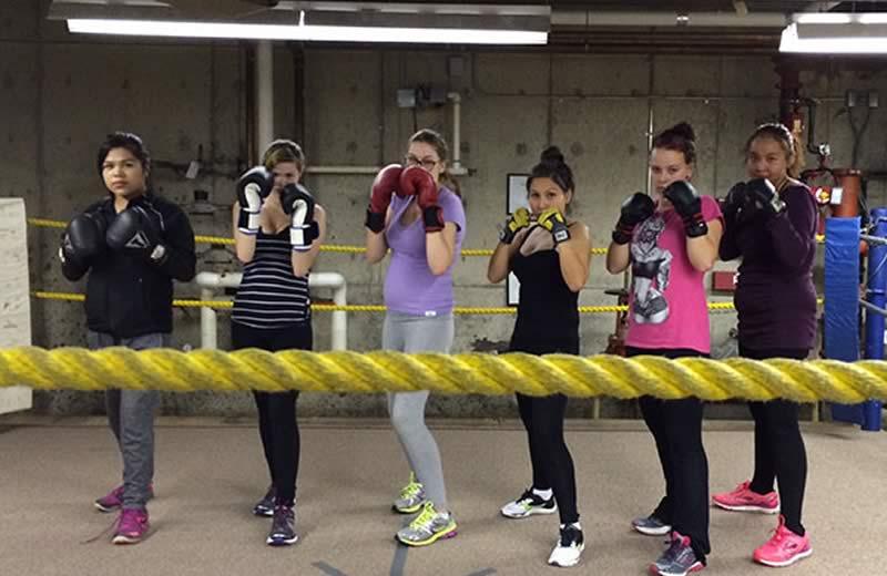 Group of 5 female teens in a boxing ring wearing boxing gloves.