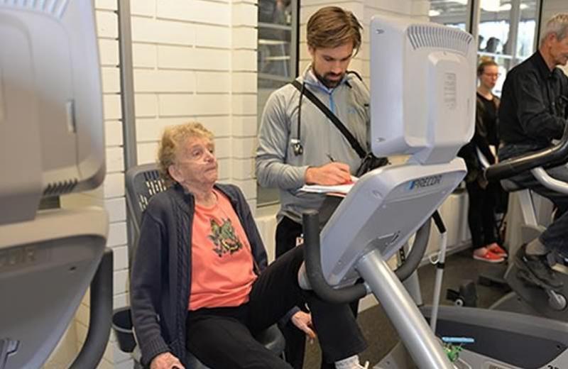 Patient on exercise bicycle monitored by physiotherapist.