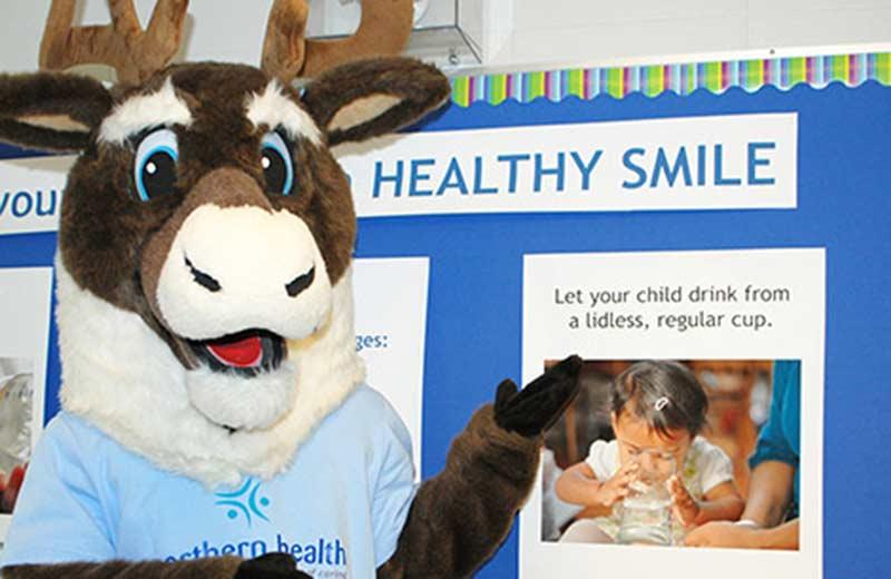 Caribou mascot in front of oral health poster.