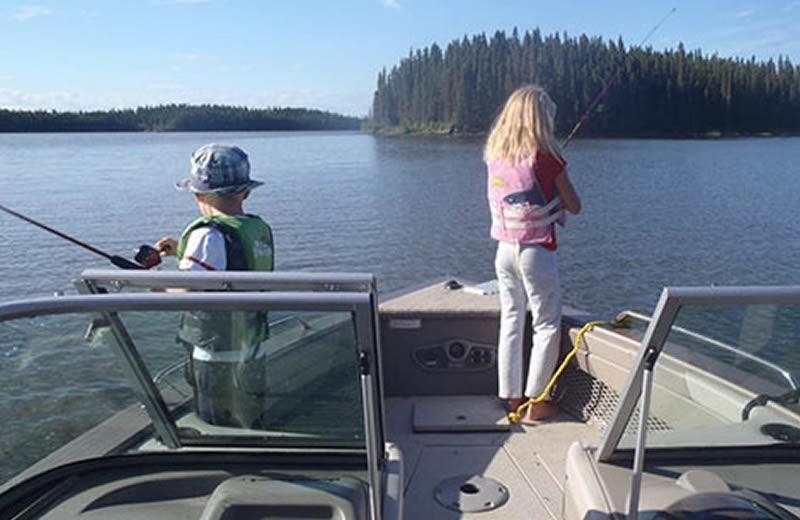 A young boy and girl standing at the front of a boat fishing.