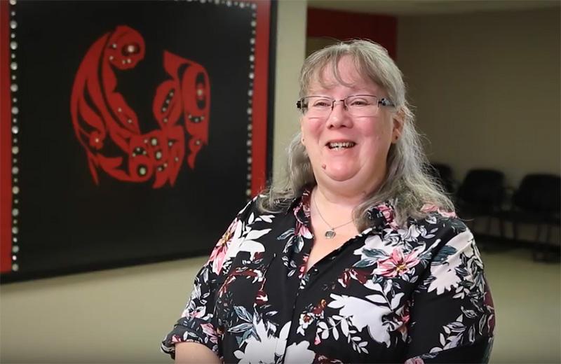 A woman sits in a room with Indigenous artwork in the background.