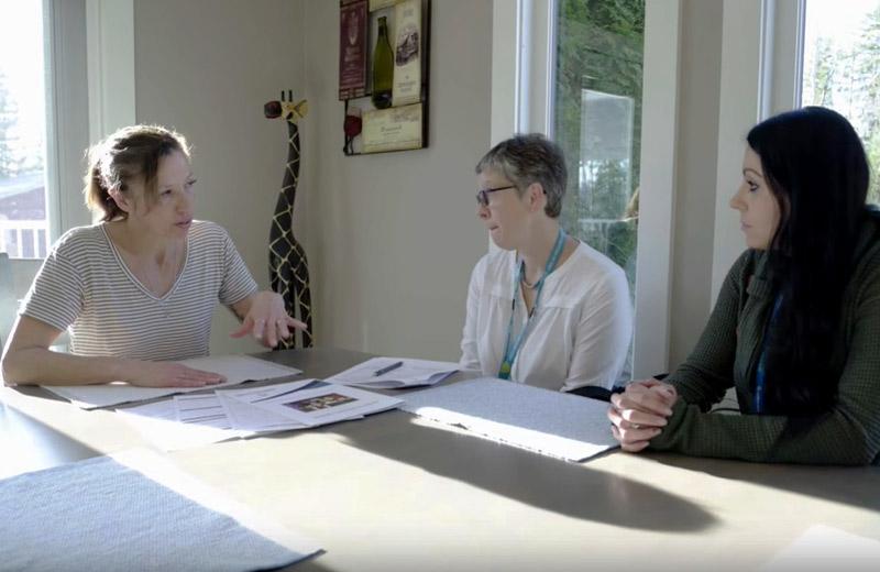 Three women sit around a table discussing care. 