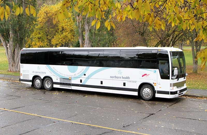 A Northern Health Connections charter bus in a parking lot. The trees in the background are gold.