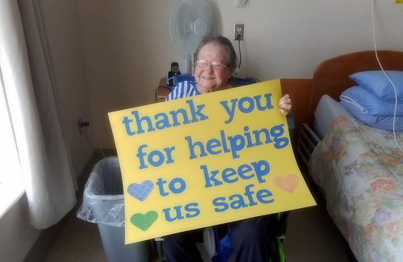 A female long-term care resident holds a sign that says, "thank you for helping to keep us safe." 