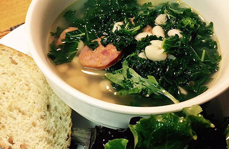 Bowl of kale, white bean and sausage soup served with bread and salad
