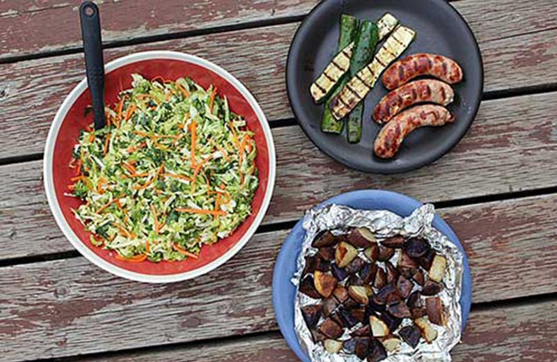 Picnic table with three BBQ dishes of food; salad, roasted potatoes and sausages