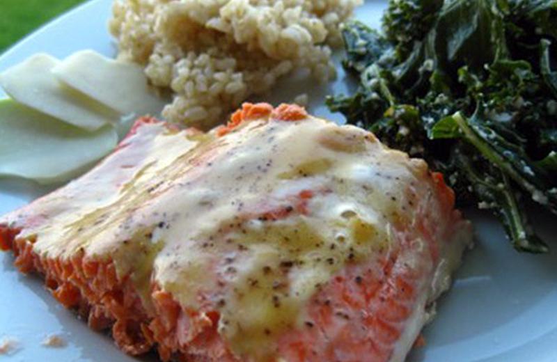 Salmon filet with Dijon sauce served on white plate with greens and rice