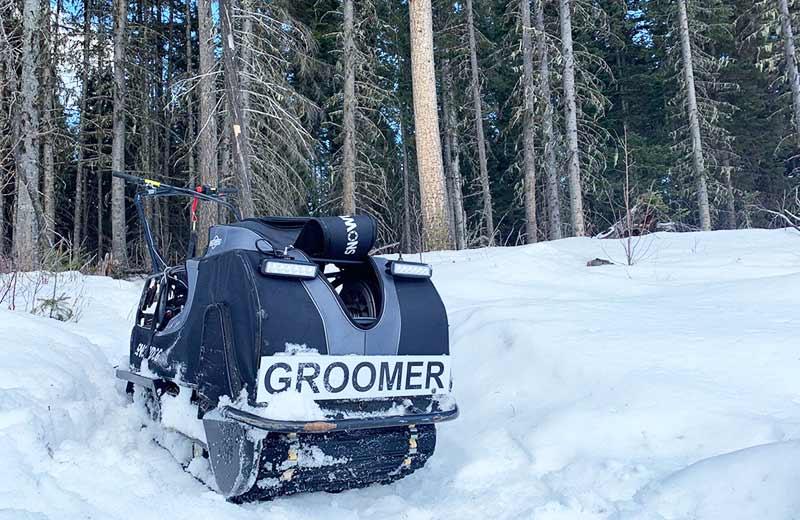 A trailer groomer sits on snow in a forest.