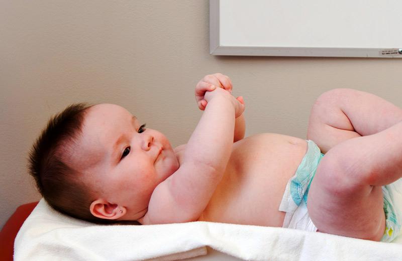 A baby wearing a diaper lays on a scale.