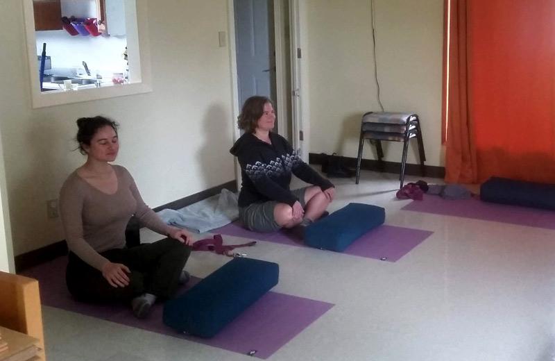 Two women sit cross legged, practising yoga. 
