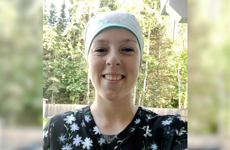 A young woman wearing medical scrubs and cap smiles into the camera.