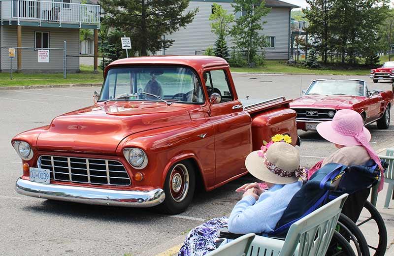 An old red pickup truck drives past two women in wheelchairs.