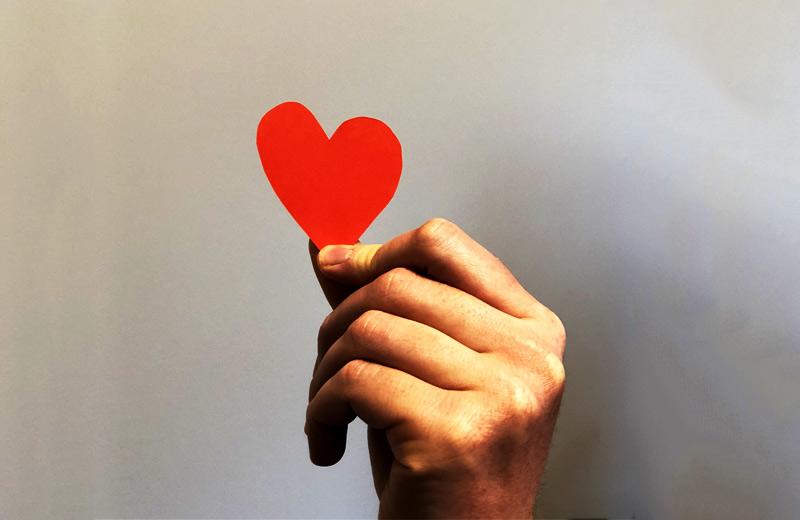 A hand holds a red construction paper heart.  