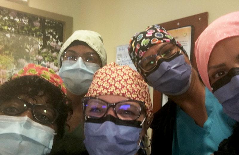 Five health care workers wearing masks and caps look into the camera.