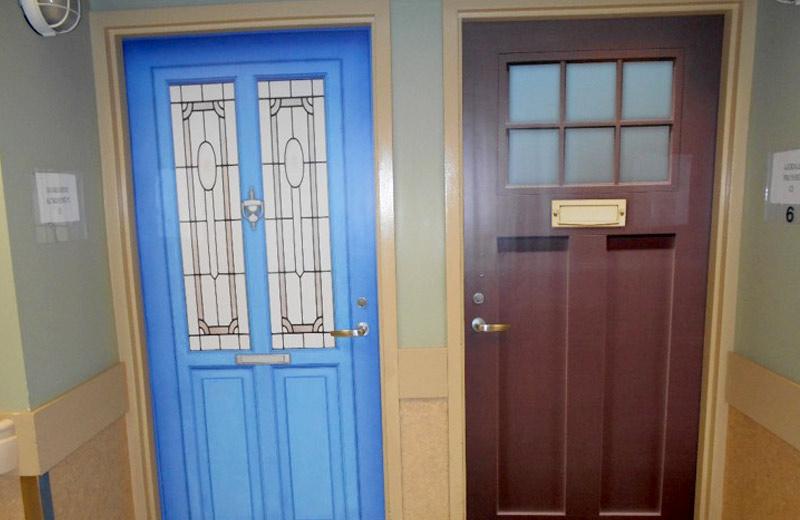 Two doors with different fake veneers. One is bright blue with long vertical windows. The other is brown with six small square windows near the top. 