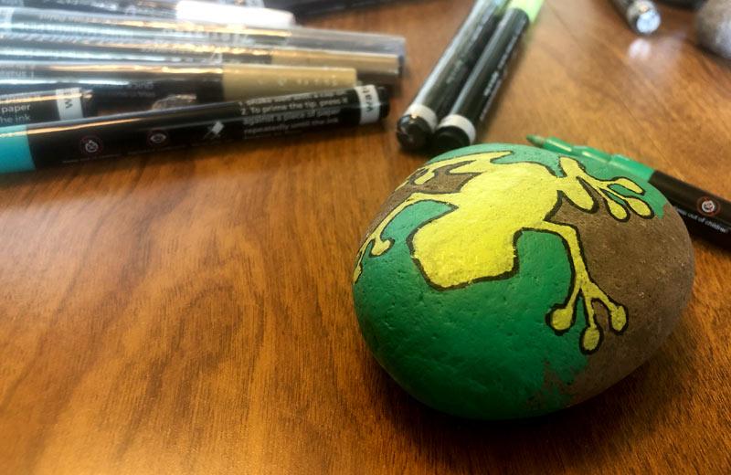 A rock has a yellow frog painted on it.