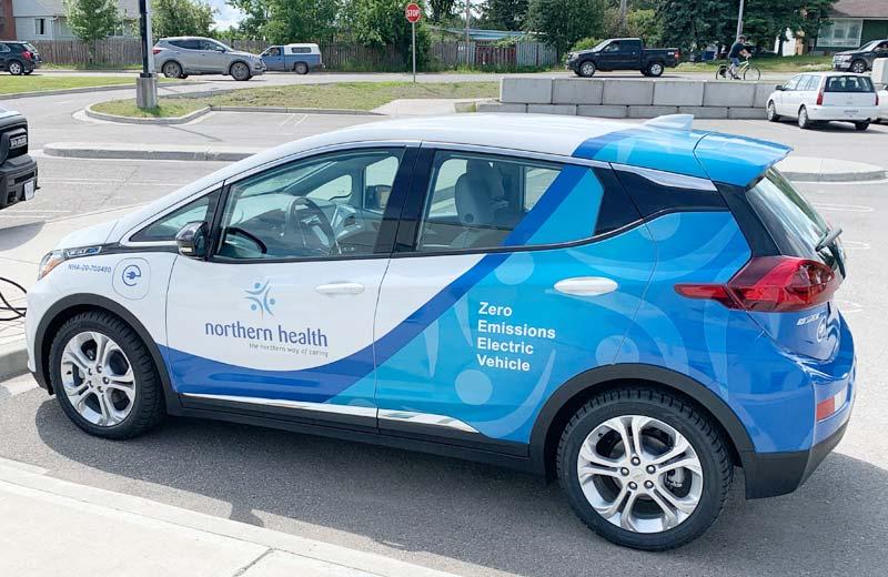 A Chevrolet Bolt with Northern Health decals is parked at a charging station.